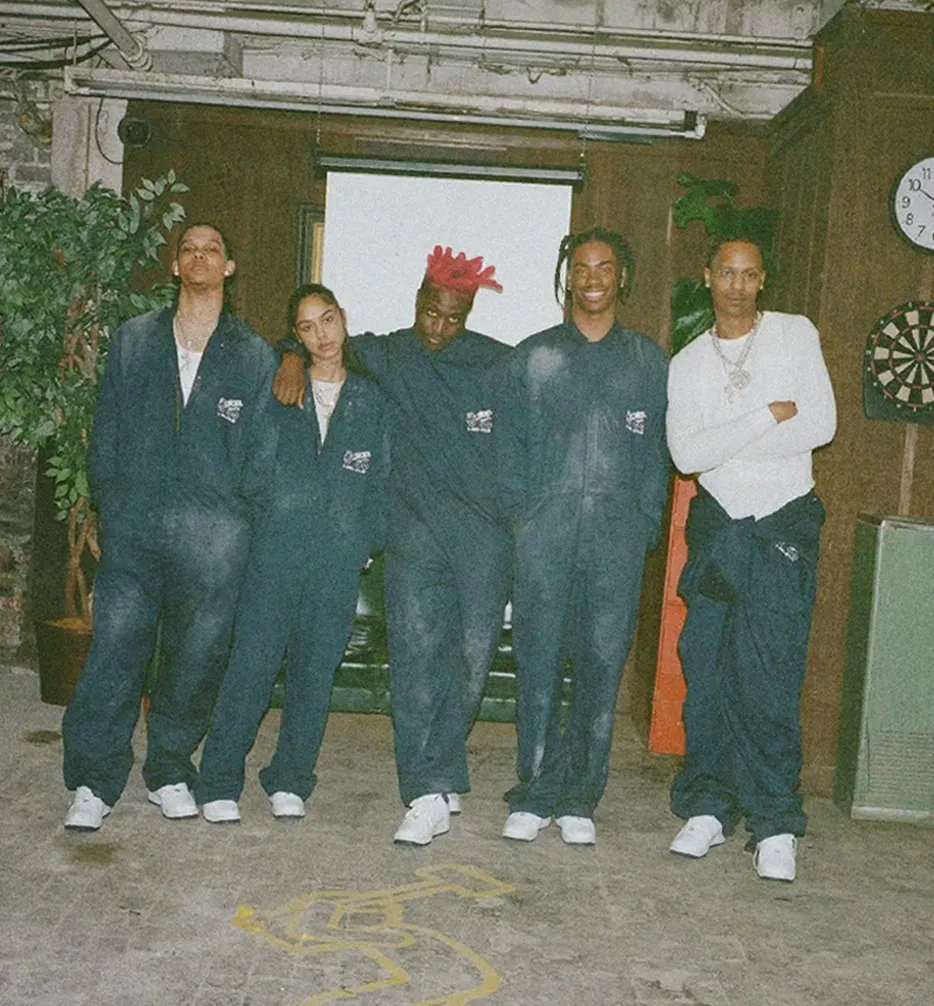 Lil Yachty and the Concrete Boys in navy Concrete Boys work suits, in a wood-panelled room
