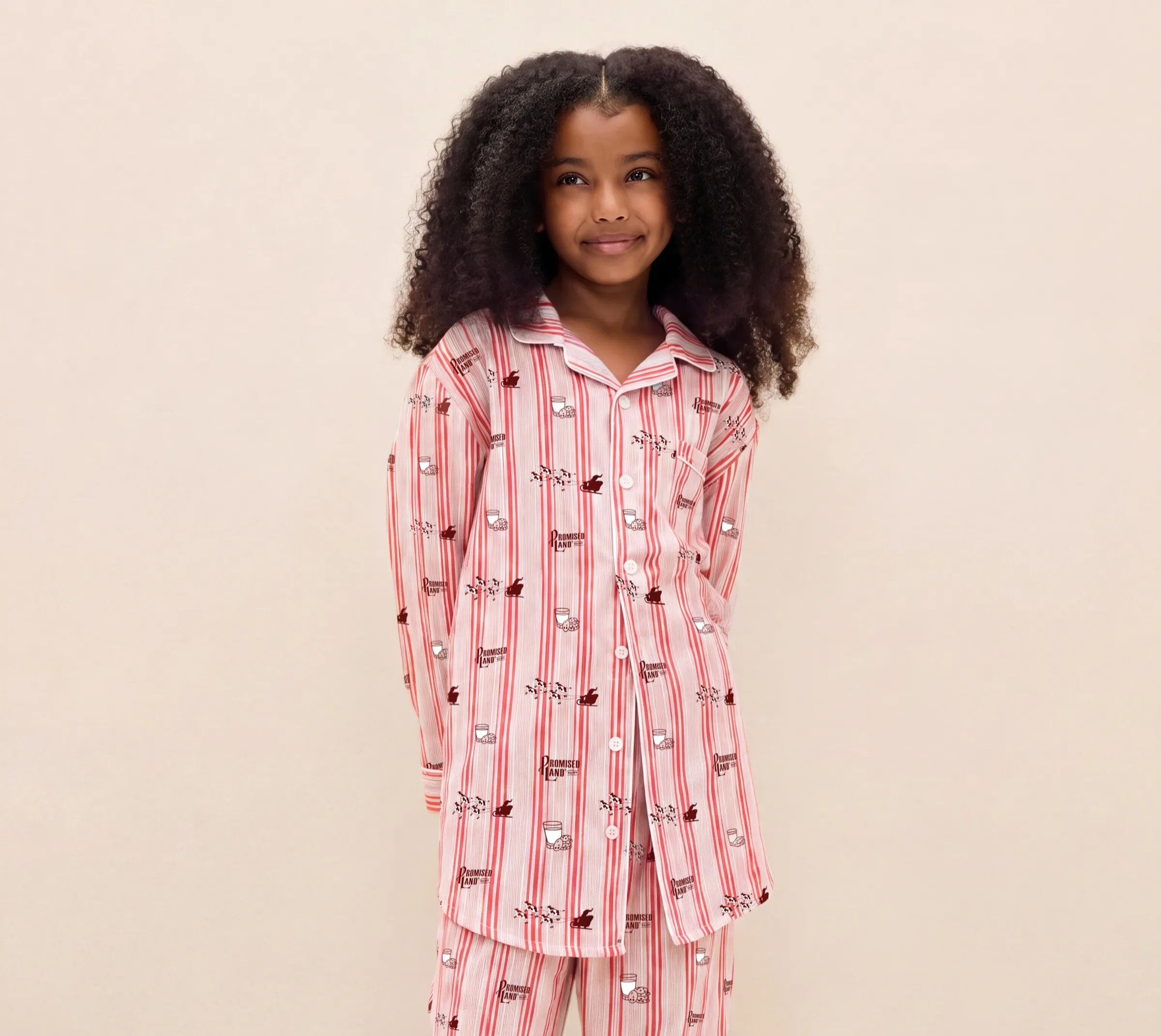 Girl in pink striped Promised Land Dairy pajamas printed with cows, sleighs, and milk and cookies