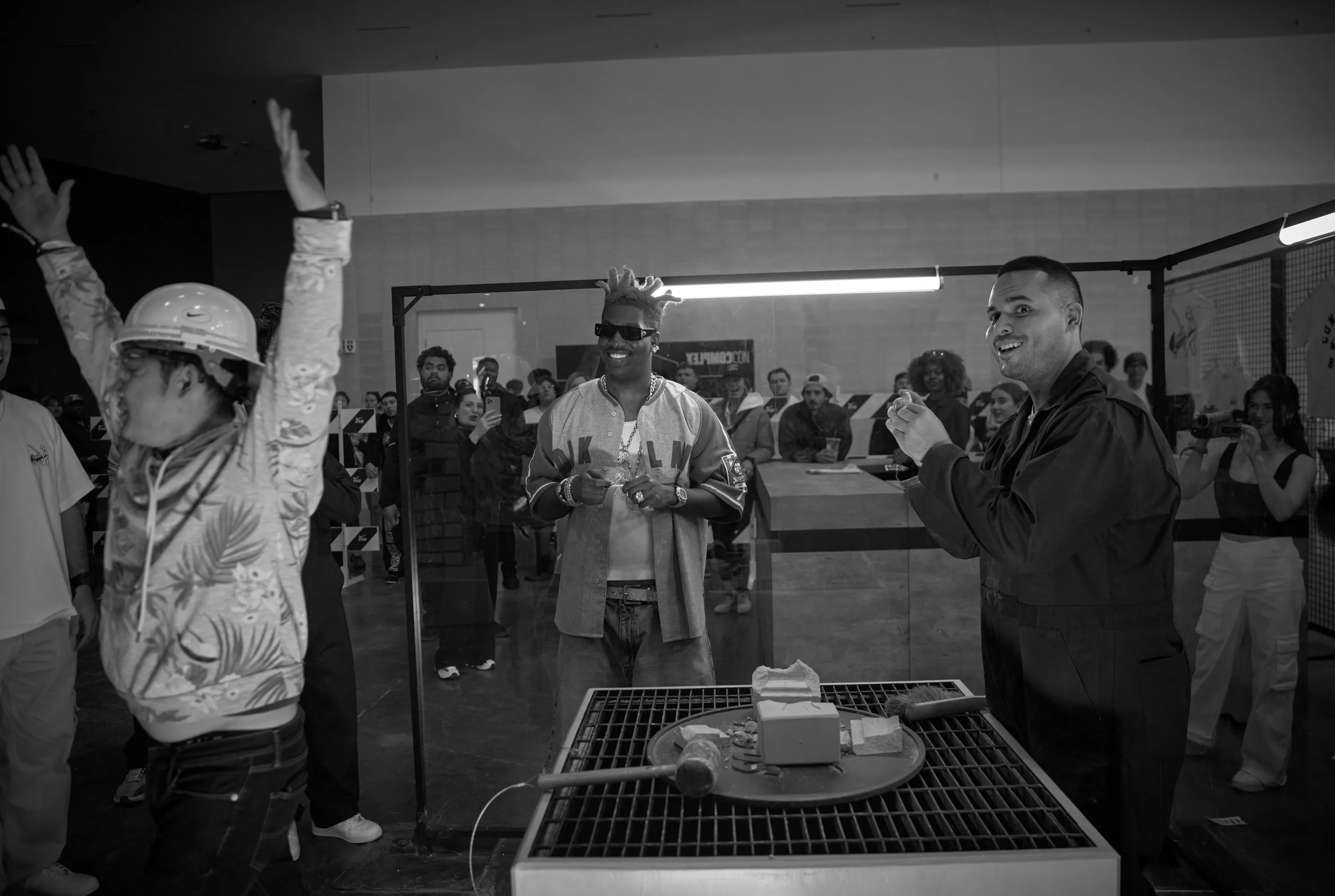 A fan in a hard hat, arms up, at the smash table, Lil Yachty grinning behind, in black and white